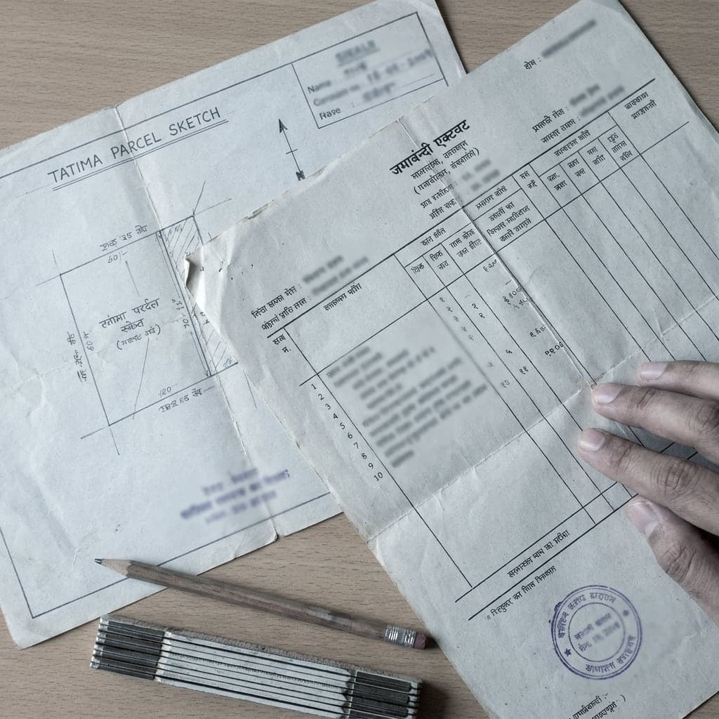A tatima parcel sketch and a jamabandi record of rights laid on a table with a pencil and a folding rule